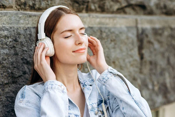 Genç Bir Öğrenci Sokakta Duvara Yaslanmış Kulaklıkla Müzik Dinliyor — Stok fotoğraf