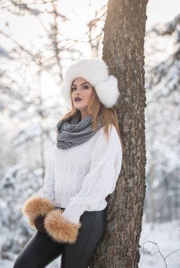 Ormandaki kış manzarası zevk aşırı büyüklükteki kürk kapaklı beyaz kazak güzel kadın. Sarışın kız karla kaplı ağaçların dalları altında poz. Çekici genç bayan parlak soğuk günde, makyaj