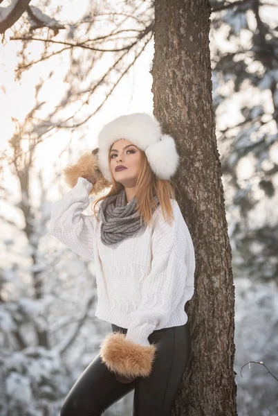 Ormandaki kış manzarası zevk aşırı büyüklükteki kürk kapaklı beyaz kazak güzel kadın. Sarışın kız karla kaplı ağaçların dalları altında poz. Çekici genç bayan parlak soğuk günde, makyaj