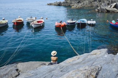 Riomaggiore sahil. Kız geri, kayaların üzerinde oturur ve tekneler ve deniz görünümünü sahiptir.