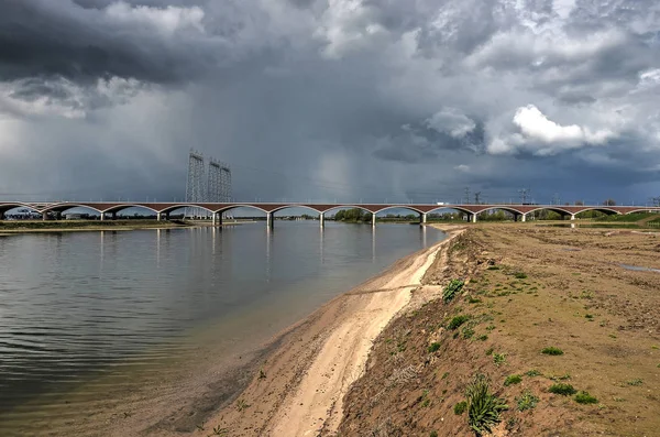 Dark clouds over the new channel in the floodplains near Nijmegen, the Netherlands, with the concrte and brick arches of bridge De OVersteek in the background