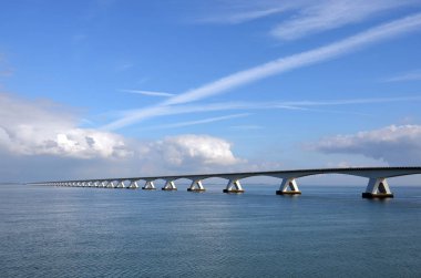 Zeeland Bridge and Oosterschelde estuary in the Netherlands, under a predominantly blue sky with some comulus clouds approaching clipart