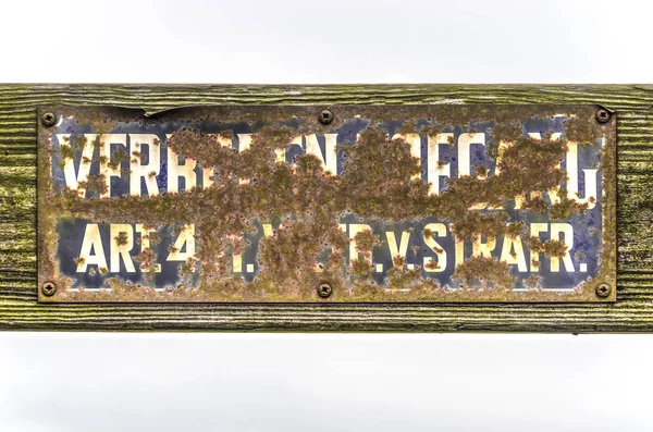 Old Dutch forbidden entry sign, its words rendered almost unreadable trough rust and dirt, on a wooden suface