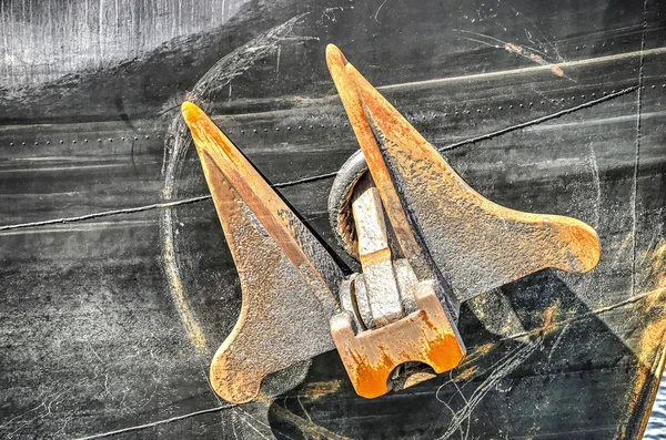 Large rust-colored anchor attached to the black hull of a ship near the stem