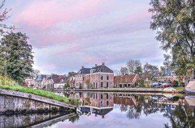 Leeuwarden, Hollanda, 3 Kasım 2018: Snakkerburen Mahallesi'nde eski evleri Dokkumer Ee kanal mor gökyüzü altında sakin suda günbatımında yansıtacak