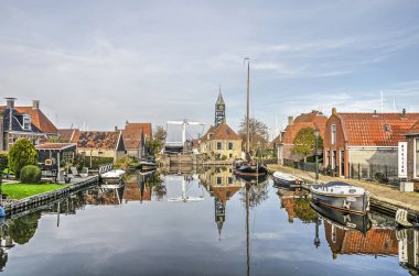 Hindeloopen, The Netherlands, November 4, 2018: sluice and adjacent sluice keepers house, bridge, boats and old houses reflect in the mirror-like water surface of a canal on a windless day clipart