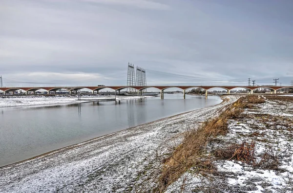 View from the north bank of the new channel of the river Waal near Nijmegen, The Netherlands with city bridge De Oversteek (The Crossing) in the background, on a cold day in winter