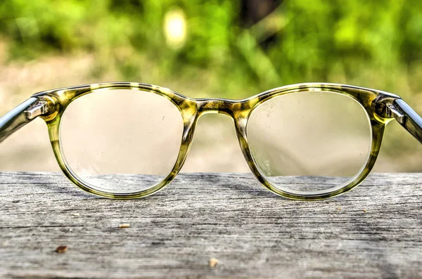 Reading glasses in a plastic frame on a rough wooden surface against a grain background