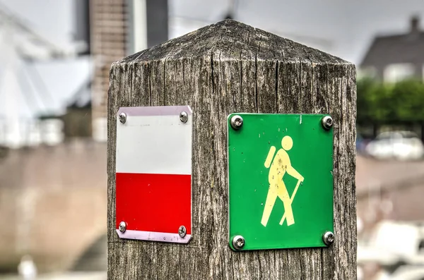 在模糊的背景下 带有红白的长途小径标志和绿色黄色徒步标志的风化木杆 — 图库照片