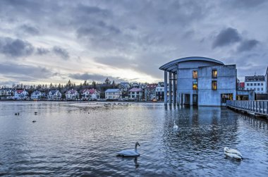 Reykjavik, Izlanda, 27 Şubat 2019: Belediye Binası, bitişik banliyö mahalle ve göl Tjornin altında dramatik bir gökyüzü altında şafak