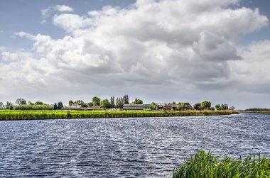 De Donk mezrası ilkbaharda bulutlu bir gökyüzü altında Hollanda'da Alblasserwaard polder bir kanalın kıyısında düşük bir nehir kumul üzerine inşa