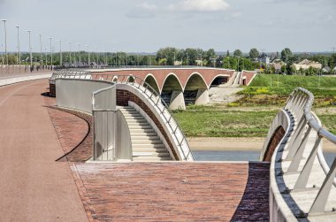Nijmegen, Hollanda, 25 Nisan 2019: Zarif kıvrımlı merdivenler De Overstek köprü güvertesinden sel ovasındaki peyzaj parkına doğru iniyor
