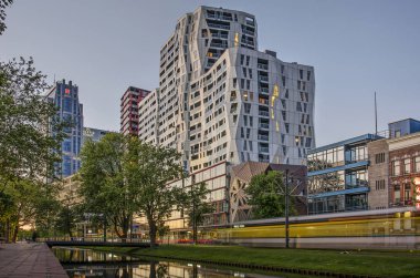 Rotterdam, Hollanda, 12 Mayıs 2019: Westersingel kanalının yeşil kıyısının görünümü gece olmadan kısa bir süre önce geçen bir tramvay ve Calypso apartmanı ile 