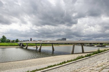 Nijmegen, Hollanda, 25 Nisan 2019: Dramatik bir gökyüzü altında Waal nehri yeni kanal üzerinde Lentloper köprü doğru taş döşeli Lentse Warande nehir kıyısından görünümü