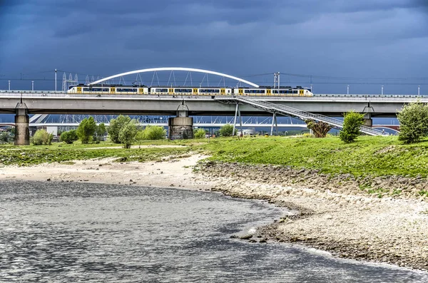 荷兰尼梅根 2019年4月25日 瓦尔河畔的沙 草和岩石 在乌云的天空下 背景中各座桥梁 — 图库照片