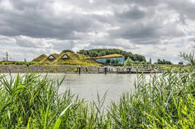 Werkendam, Hollanda, 3 Temmuz 2019: toprakla kaplı Biesbosch müzesine, restorana ve iskeleye doğru su üzerinde sazlıklar arasında bir manzara