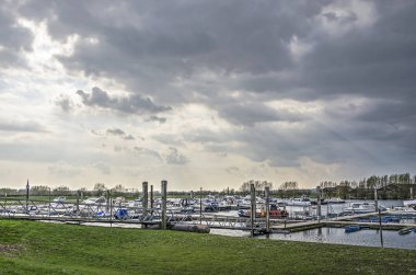 Doesburg, Hollanda, 30 Mart 2019: İlkbaharda dramatik bir gökyüzü altında Ijssel nehrinin eski bir bölümünde küçük yatlar ile marina