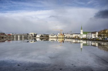 Reykjavik, İzlanda, 23 Şubat 2019: Belediye binası ve Frikirkja kilisesi arasındaki Tjornin Gölü'nün kuzey kıyısındaki tarihi şehir merkezi eriyen buzu yansıtıyor