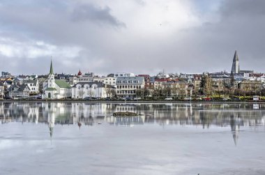 Reykjavik, İzlanda, 23 Şubat 2019: Frikirkja ve Hallgrimskirkja kiliseleriyle tjornin Gölü'nün doğu kıyısında dramatik bir gökyüzünün altındaki buzda yansıtılıyor