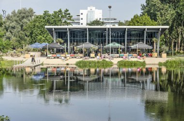 Zwolle, The Netherlands, July 28, 2019: iew across a pond towards the pavillion in Wezenlanden park with its own beach and jetty clipart