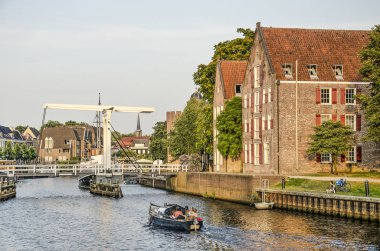 Zwolle; The Netherlands; July 24; 2019: little boat cruising in Thorbecke canal, approaching a drawbridge and historic houses, on a summer evening clipart
