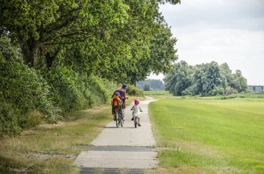 Vollehove, Hollanda, 4 Ağustos 2019: genç baba, bir çocuk koltuğunda, kendi bisikletinde, beton bir yolda, orman ve çayırlarda bir çocukla bisiklete binerek