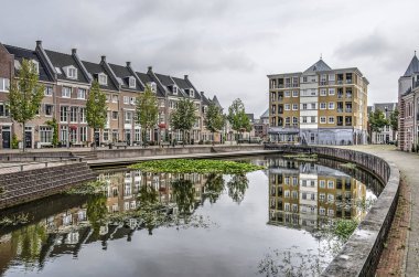 Helmond, The Netherlands, August 16, 2019: houses build in a neoclassist style in postmodern neighbourhood Brandevoort reflect in the pond on the central square clipart