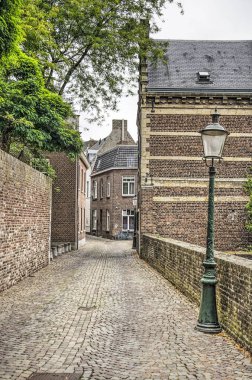 Maastricht, Hollanda, 8 Eylül 2019: tuğla duvarlar ve evler, bir fener ve bir ağaç ile eski şehirde dar bir sokak boyunca görünümü
