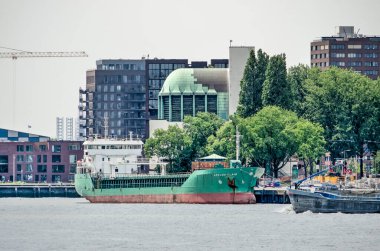 Rotterdam, Hollanda, 6 Haziran 2020: Park 'ın ağaçlarında yeşilin çeşitli tonları, denize giden bir gemi ve Maastunnel havalandırma binasının patentli bakırı. 