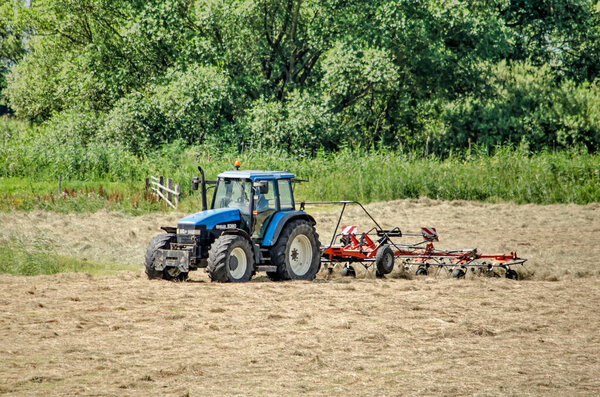 Wilsum, The Netherlands, July 21, 2020: agricultural machine at work in a field of drying hay