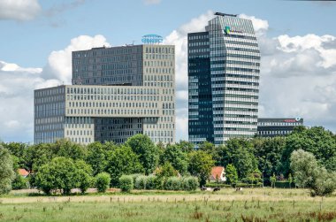 Zwolle, The Netherlands, July 21, 2020: long distance view of two large modern office buildings at Voorsterpoort area, with a contrasting rural landscape in front of them clipart