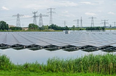 Zwolle, Hollanda, 19 Temmuz 2020: büyük bir dizi güneş paneli, arka planda elektrik direkleri ve elektrik hatlarıyla yapay Sekdoorne Plas gölüne yansıyor.