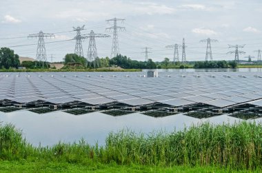 Zwolle, The Netherlands, July 19, 2020: a large array of solar panels reflects in the artificial lake Sekdoorne Plas, with electricity pylons and power lines in the background clipart