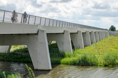 Kampen, Hollanda, 26 Temmuz 2020: IJssel nehrinin taşmasını önlemek için yeni Reevediep nehir kanalı üzerindeki beton bir köprüde iki bisikletçi