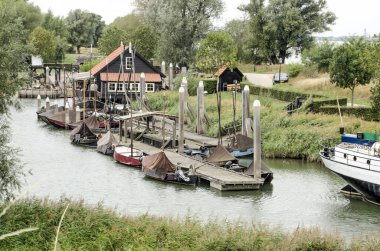 Woudrichem, Hollanda, 23 Eylül 2020: Ahşap binaların manzarası ve eski kasabanın tahkimatlarının hemen dışındaki yeşil bankaların bulunduğu bir kanalda küçük tekneli bir iskele.