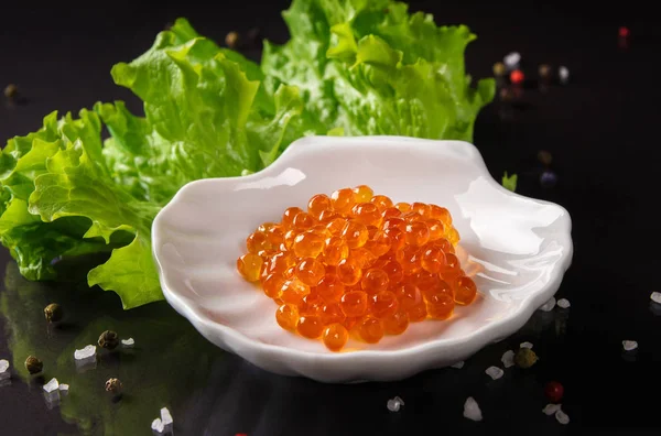 siyah arka plan üzerine beyaz daire kırmızı somon havyar ve salata ile yatay fotoğraf bırakır