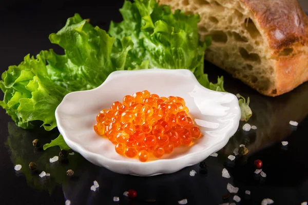 yatay fotoğraf kırmızı somon havyar ile beyaz daire salata yaprakları ve siyah arka plan üzerine ekmek