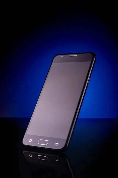 standing upright smartphone on reflective surface with blue light on background