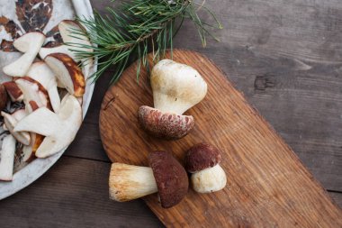 Ahşap kesme tahtası üzerinde yalan üç çörek mantar dilimlenmiş mantar bir tabak ve eski ahşap bir masa üzerinde bir çam dalı.