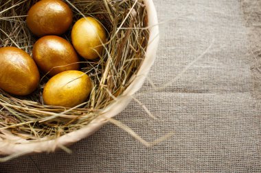 Altın yumurta samanla söğüt dalları üzerinde dokuma bir arka plan ile sepet içinde görünüm üst. Paskalya kompozisyon. Kopya alanı