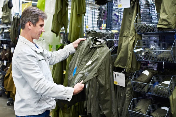 Man chooses raincoat for fishing in sports store — Stock Photo, Image