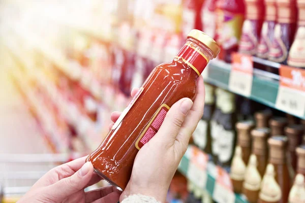 Buyer hands with bottle of chilli sauce in store