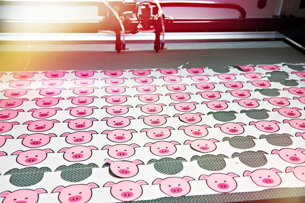 Drawings of piglets on fabric in machine for cutting — Stock Photo, Image