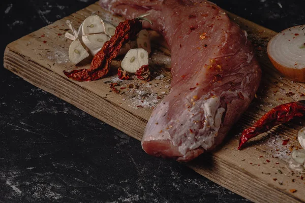 Frisches rohes Schweinefilet auf Holzschneidebrett mit Zwiebel, Knoblauch und Messer auf dunklem Hintergrund und Leerraum für Ihren Text — Stockfoto