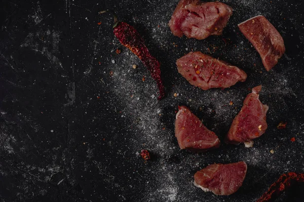 Stücke rohes Schweinemedaillons-Steak mit Gewürzen, Salz und Pfeffer auf dunklem Stabhintergrund im rustikalen Stil, Ansicht von oben — Stockfoto