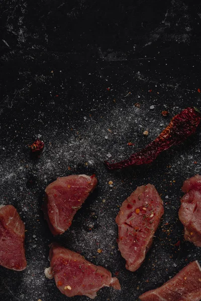 Frisches rohes Schweinemedaillonfleisch mit Gewürzen, Salz und Pfeffer auf dunklem Steinhintergrund, Leerraum für Ihren Text, Kopierpaste, Ansicht von oben — Stockfoto
