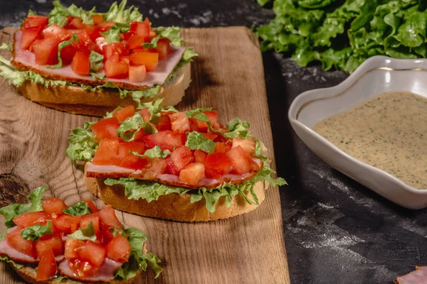 Bruschetta buatan Italia dengan tomat cincang, daun salad, ham dan saus pada roti berkerak panggang. tampilan horisontal — Stok Foto