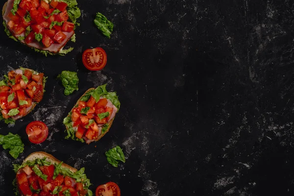 Doğranmış domates, mozzarella sos, salata yaprakları ve karanlık baton arka plan üzerinde jambon ile geleneksel İtalyan Bruschetta. Geleneksel İtalyan meze veya aperatif, meze. Ana sayfa görünümü ile kopya alanı, co