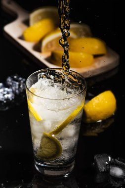 Köpüklü soğuk su Detoks limon dilimleri ve buz siyah arka bir karanlık cam zemin üzerine dökülen