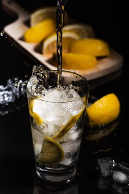 Köpüklü soğuk su Detoks limon dilimleri ve buz siyah arka bir karanlık cam zemin üzerine dökülen